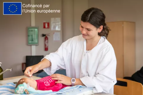 Jeune fille qui prend soin d'un bébé (poupée) lors d'un atelier pratique du CAP SAPVER