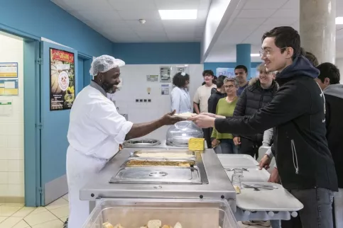 Jeune qui se fait servir un plat par le personnel du self